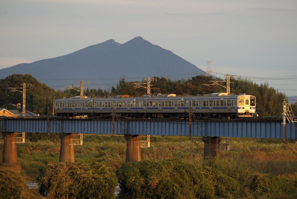 筑波山を背景に夕日に照らされながら鬼怒川橋梁を走り抜けるＪＲ水戸線列車