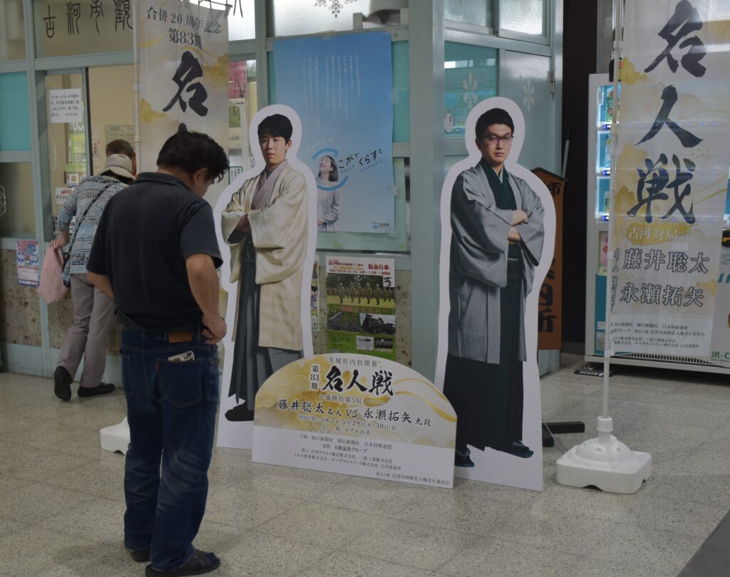 JR古河駅の観光案内所脇に立てられた対局者の等身大パネル。対局に向け機運も高まる=JR古河駅