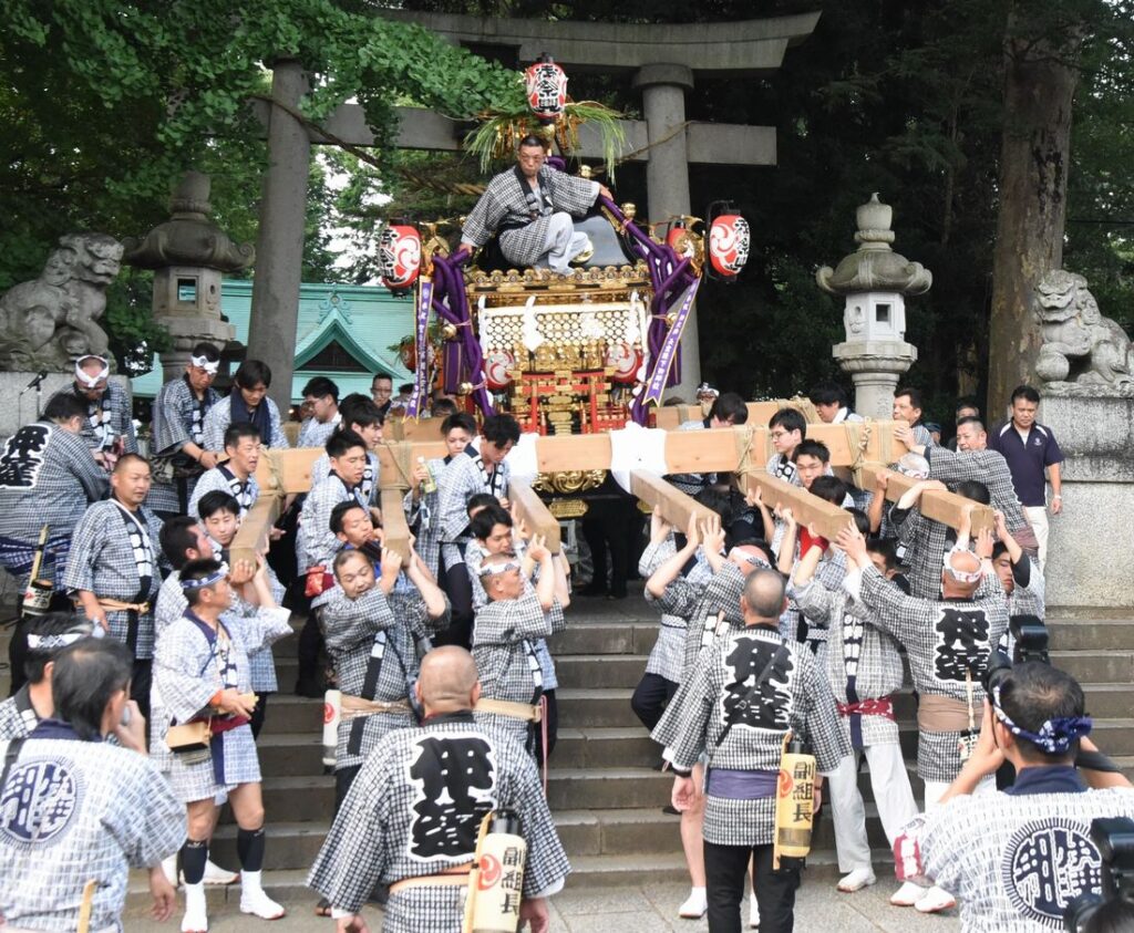 下館祇園まつりの始まりで、羽黒神社境内から繰り出す明治みこし。みこしの飾りが鳥居のしめ縄に引っ掛からないように、人が屋根に乗っています=2019年7月25日、筑西市甲