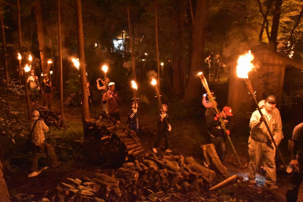 たいまつを抱えて山を登る参加者たち=2019年、桜川市真壁町山尾