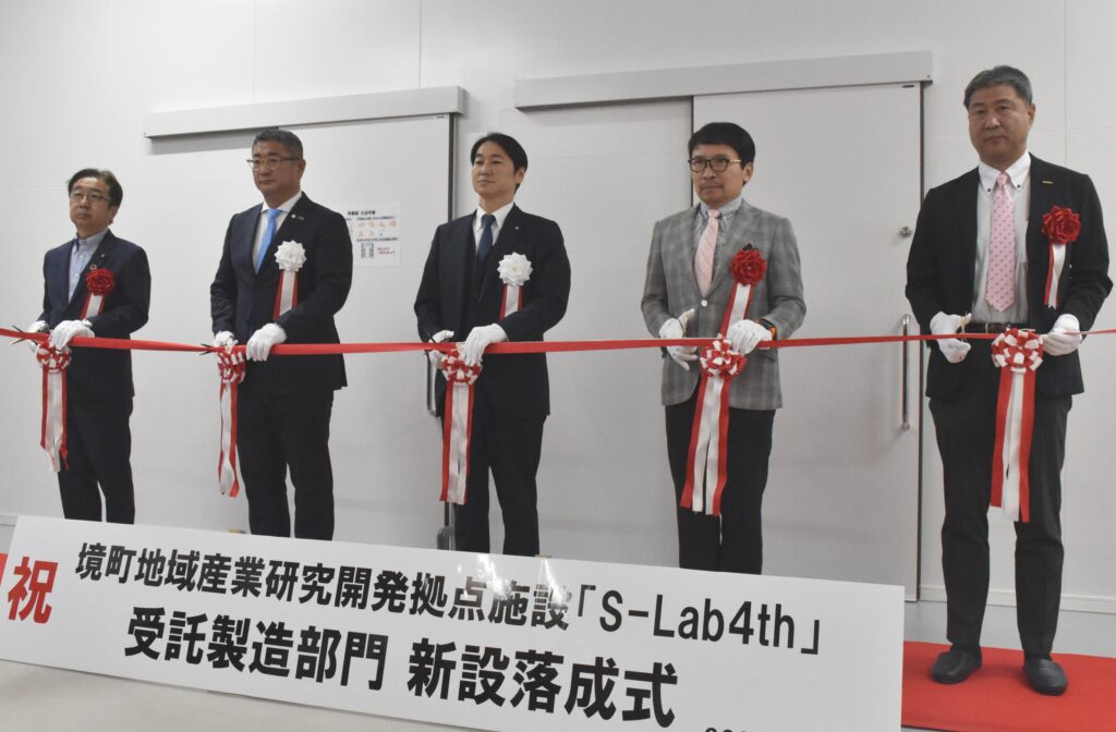 施設の完成を祝いテープカットする橋本正裕町長（右から３人目）や崔鍾植社長（同２人目）ら関係者＝境町上小橋