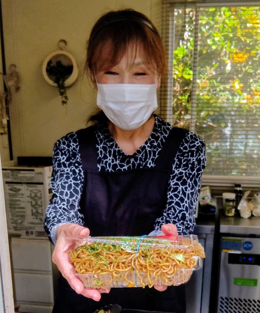 店主の谷口浩美さんとパックからあふれる焼きそば