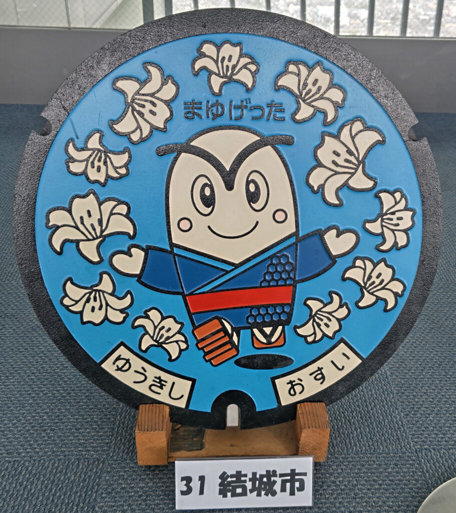 市の公式キャラクター「まゆげった」をあしらった結城市のマンホール=水戸市笠原町