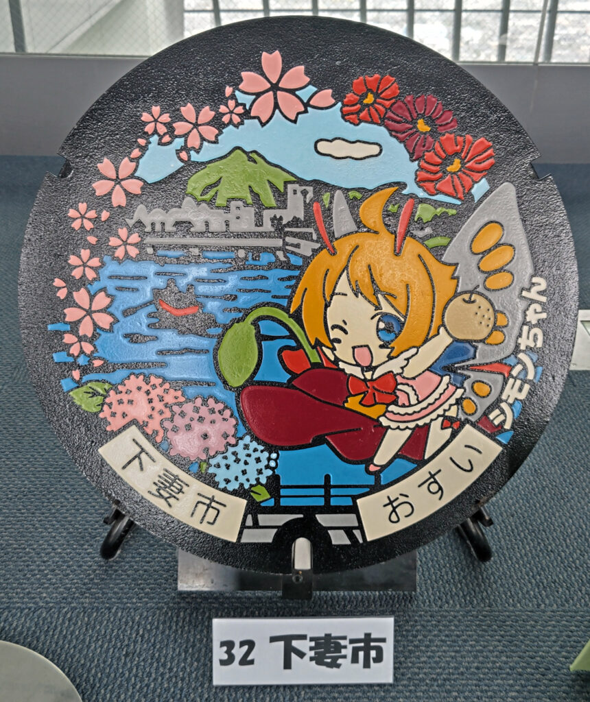 市の公式キャラクター「シモンちゃん」と花々をあしらった下妻市のマンホール=水戸市笠原町