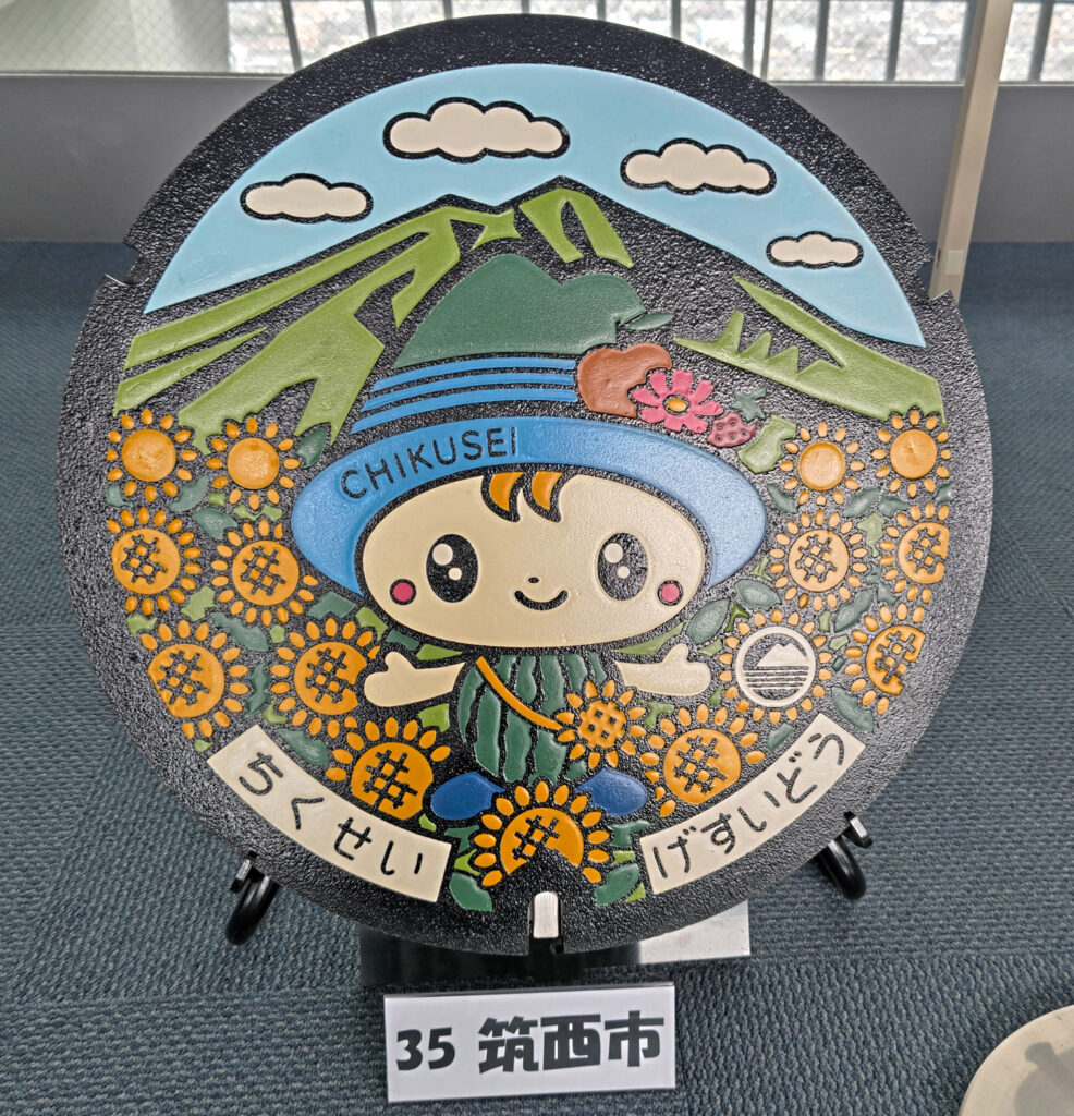 八重ひまわりと筑波山をバックに市の公式キャラクター「ちっくん」をあしらった筑西市のマンホール=水戸市笠原町
