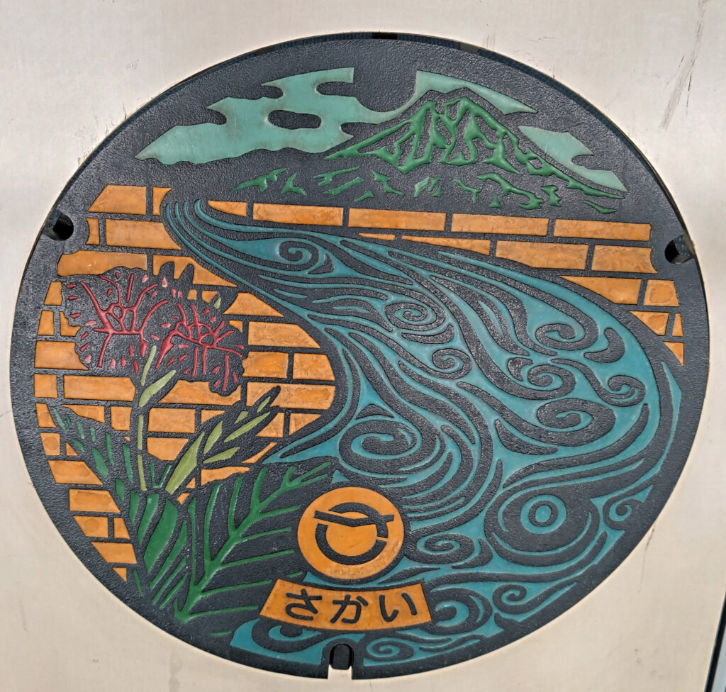 利根川を背景に町の花「カンナ」をあしらった境町のマンホール=水戸市笠原町